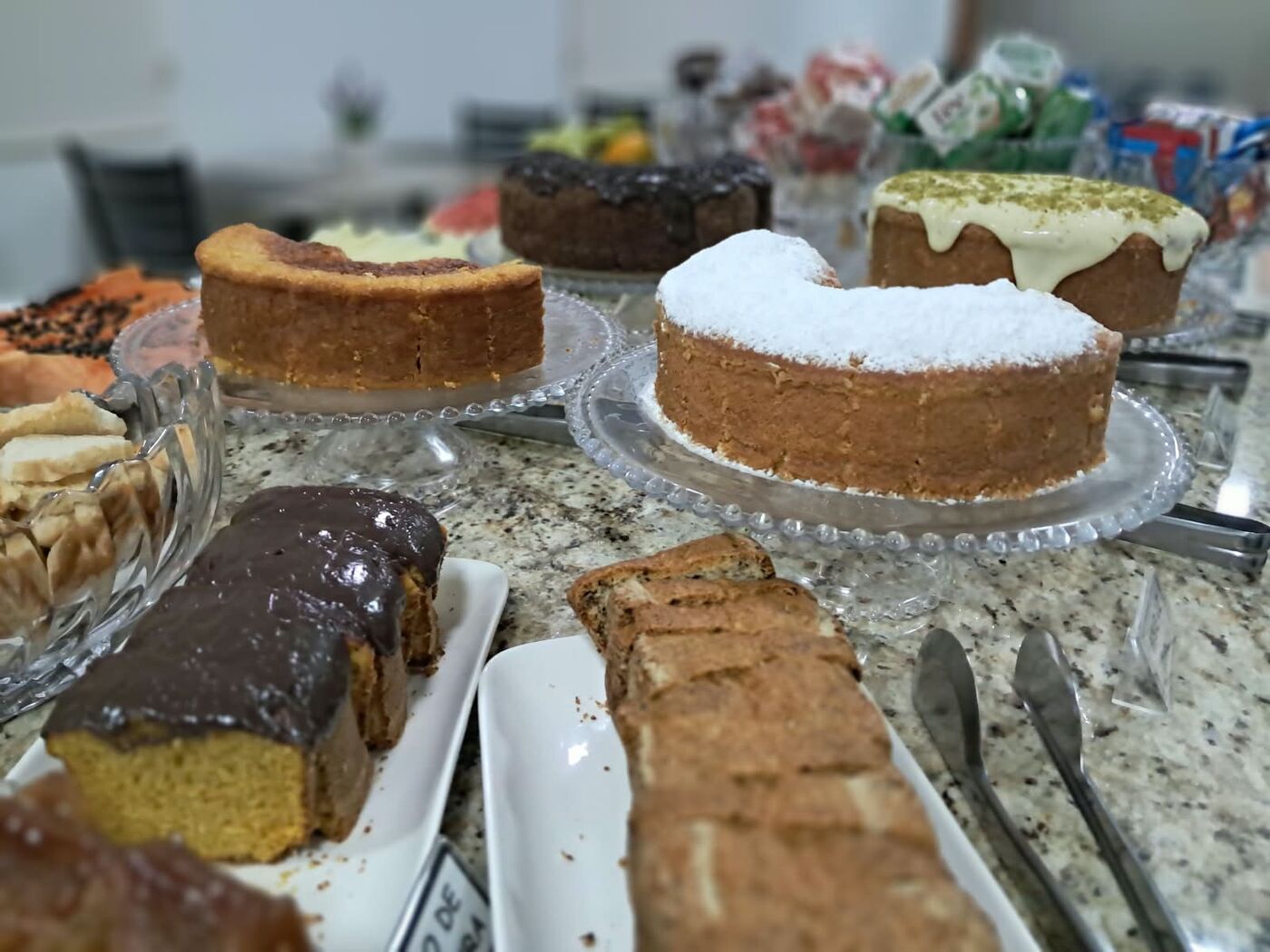 Mesa do café da manhã com vários bolos sobre boleiras de vidro