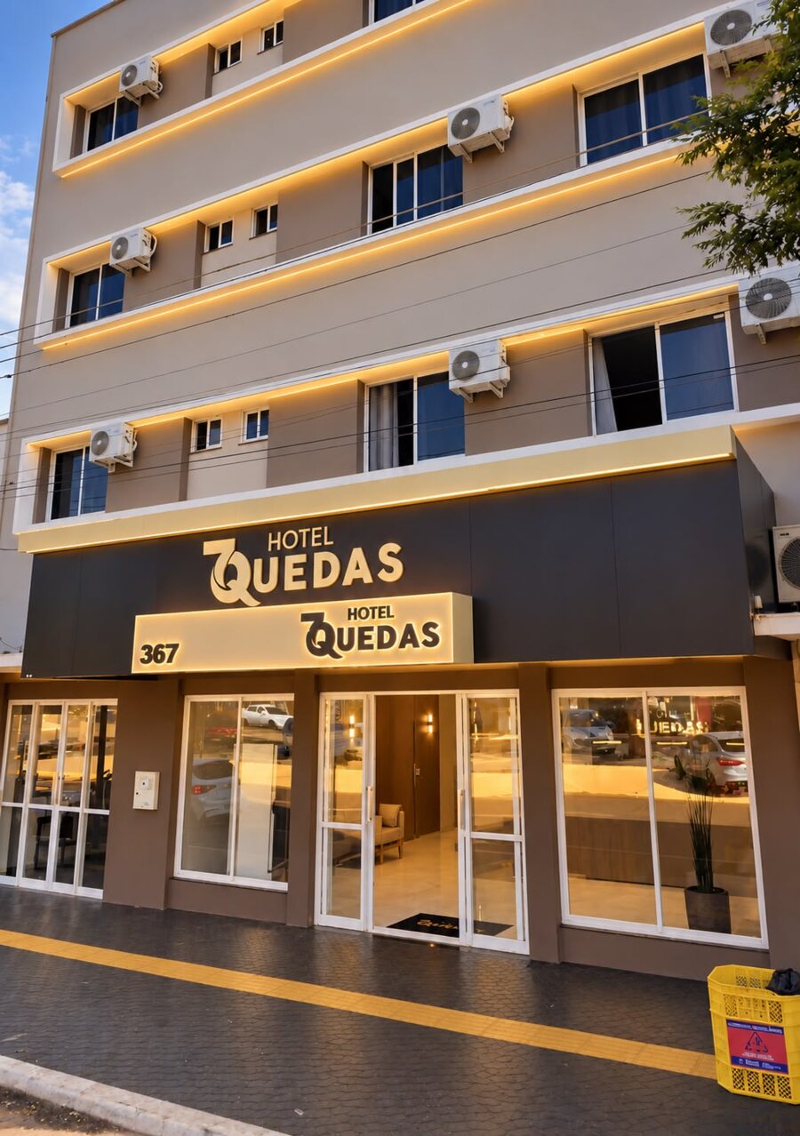 Fachada do Hotel 7 Quedas, prédio de quatro andares com faixas de luz dourada e o letreiro na entrada