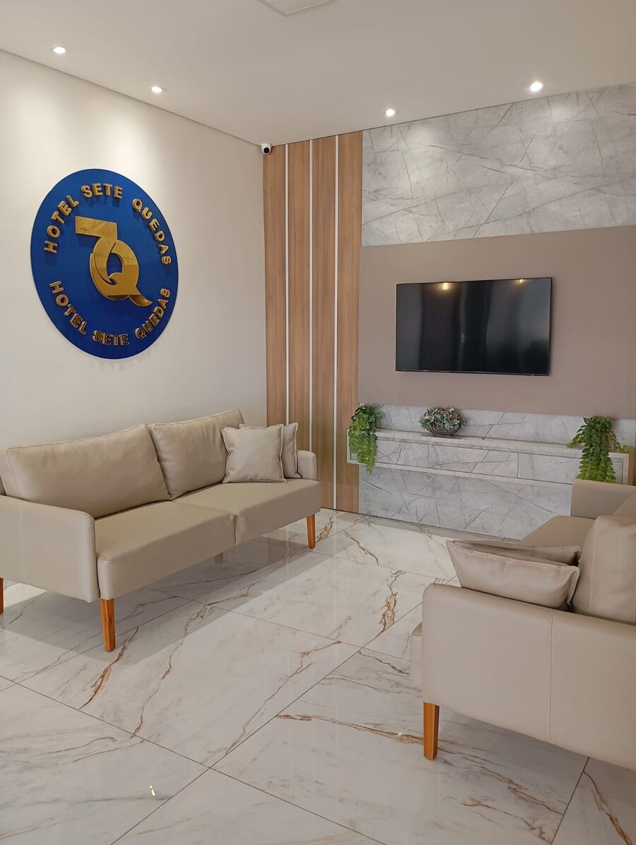 Sala de estar do hotel com sofás, TV e o brasão azul do Hotel Sete Quedas na parede