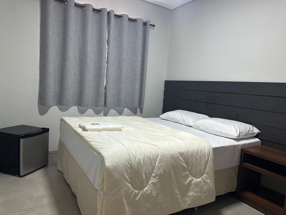 Quarto de casal com frigobar, cortinas cinza e cabeceira escura