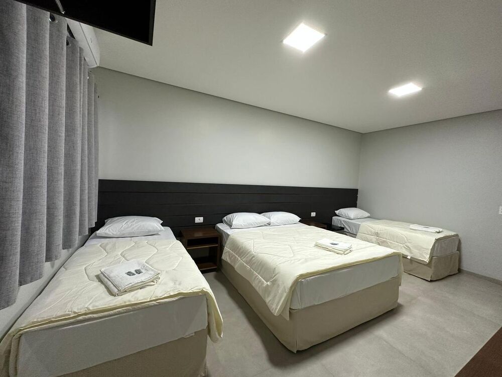 Quarto amplo com três camas, ar-condicionado e TV